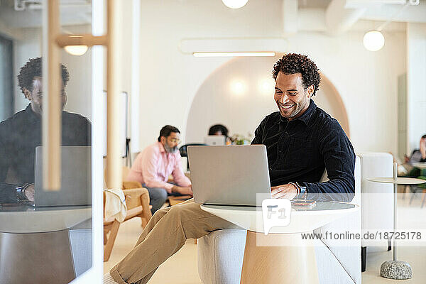 Smiling businessman using laptop while sitting on sofa at cafe