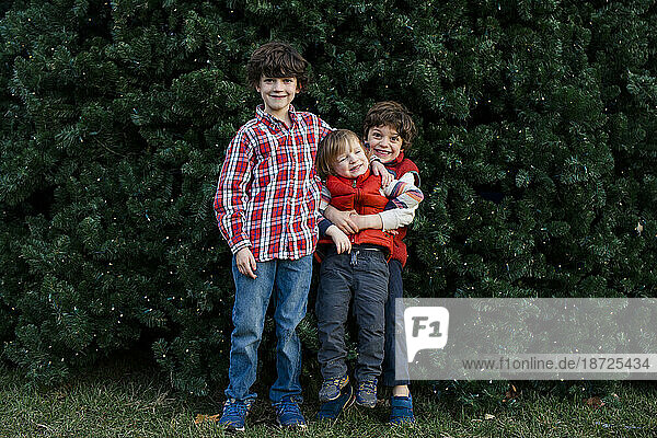 Three playful brothers stand happily together in front of tree