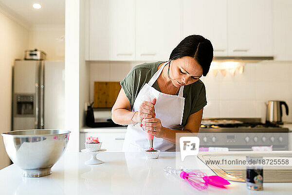 A woman decorating a cupcake with frosting in her kitchen