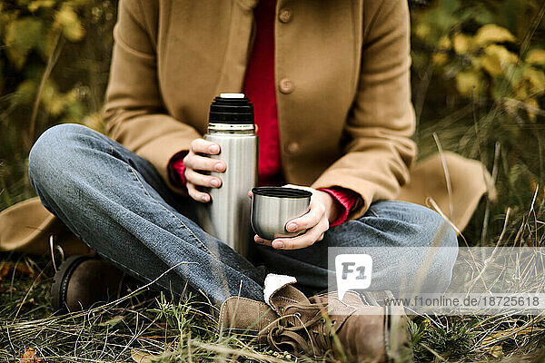 Young woman pouring tea from thermos flask into cup