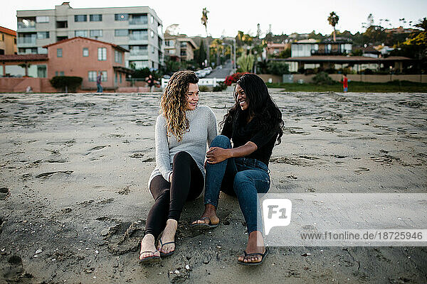 Step mom and step daughter smile at one another on beach at sunset