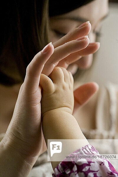 A baby girl reaches up to clasp the hand of her mother in an intimate moment in their California home.