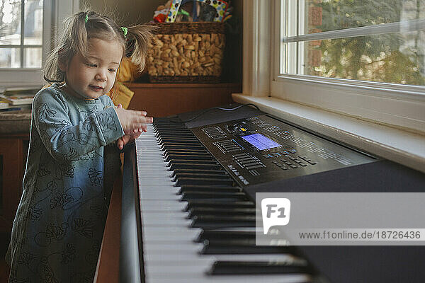 a cute little girl in pigtails plays on a keyboard in front of window