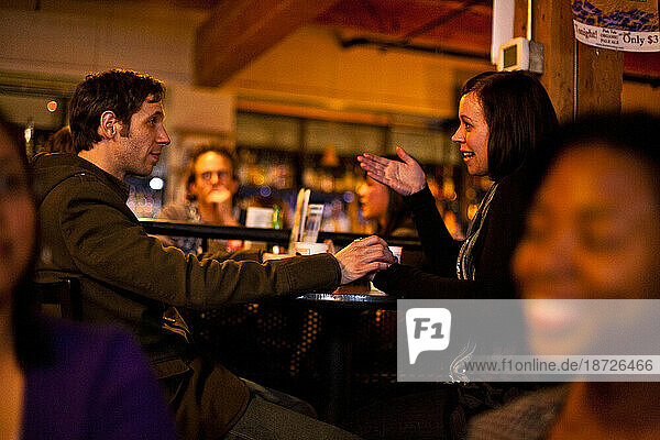 A young stylish man holds a woman's hand during a conversation in a bar in Seattle  Washington.