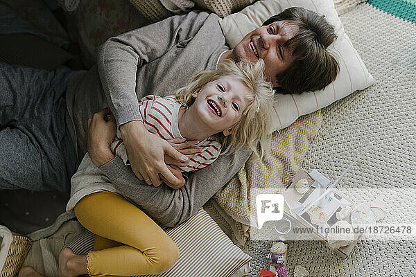 Happy father lying with daughter on pillows at home