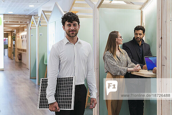 Businessman holding solar panel in office with colleagues in background