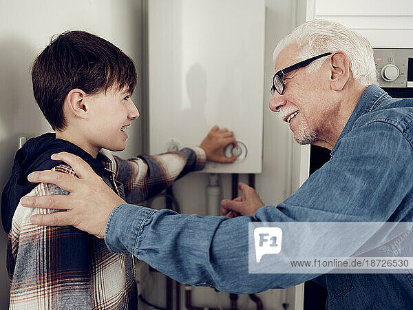 Lächelnder Enkel und Großvater passen den Heizkessel an  um zu Hause Energie zu sparen