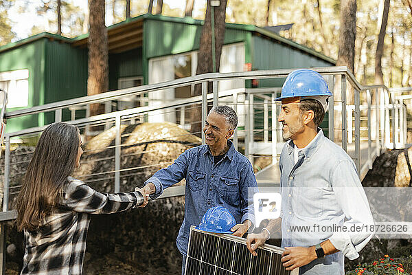 Home owner shaking hands with photovoltaic technicians carrying solar panel