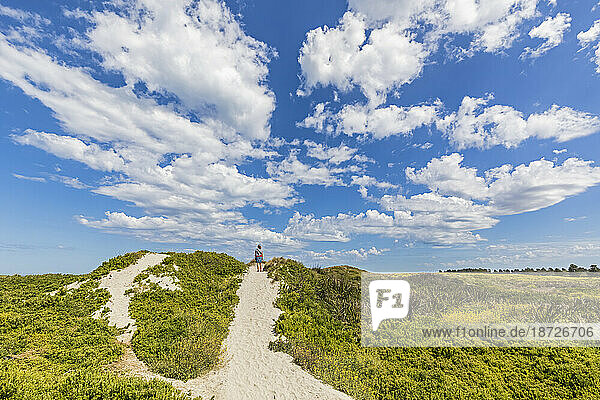 Australia  Victoria  Port Fairy  Summer clouds over female hiker standing in middle of sandy footpath in Port Fairy Coastline Protection Reserve