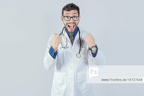 Junger Arzt freut sich über etwas  er trägt eine Brille und ein Stethoskop  er schaut mit erstaunter Miene in die Kamera