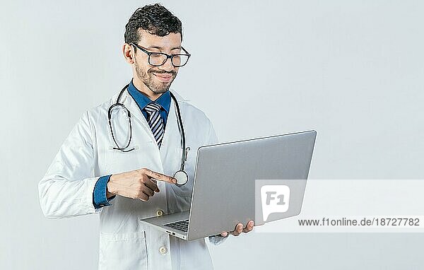 Junger Arzt mit Brille und Notebook auf isoliertem Hintergrund. Hübscher Arzt mit Laptop isoliert. Lächelnde Arzt stehend mit Laptop isoliert