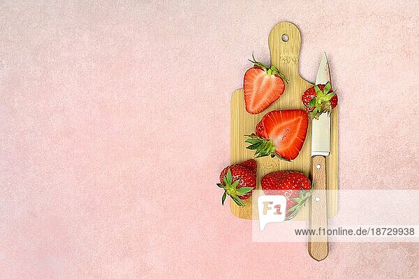 Ganze und halbierte Erdbeeren (Fragaria) mit Küchenmesser auf Holzbrett
