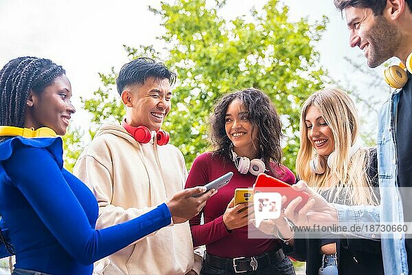 Eine Gruppe junger multiethnischer Teenager-Freunde  die auf dem Stadtcampus Handys benutzen. Das Konzept der techniksüchtigen Millennials als Gemeinschaft. Social Media Kommunikation Generation Z