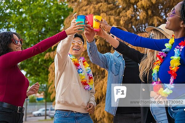 Eine Gruppe multiethnischer Freunde feiert in einem Park  Verschiedene junge Leute stoßen mit Biergläsern auf einer Sommerparty an  Happy Hour  Mittagspause und Jugendkonzept