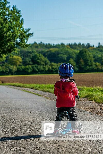 A young child with a blue bicycle helmet on a scooter
