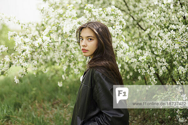 Portrait of teenage girl (16-17) against blooming apple tree
