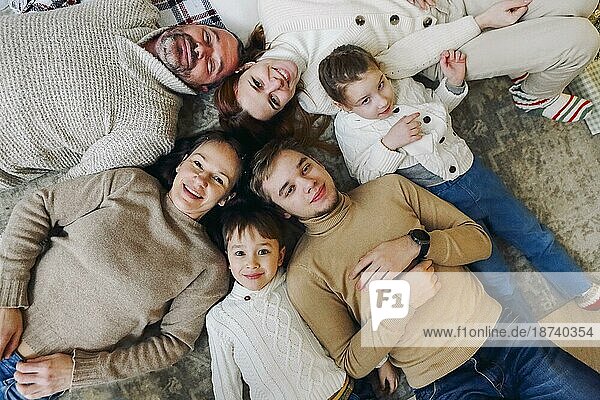 Draufsicht auf eine glückliche Mehrgenerationen Familie  die im Kreis auf dem Boden liegt und in die Kamera lächelt  um den Zusammenhalt zu stärken und von Kindheit an gesunde Beziehungen aufzubauen. Liebe und Zusammenhalt in der Familie