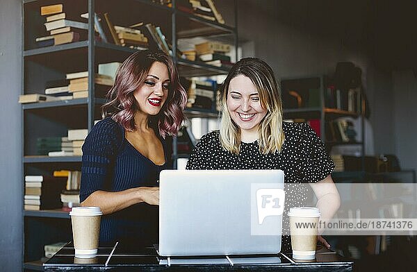 Glückliche Freundinnen lächelnd und machen Videoanruf auf Laptop am Tisch und genießen Kaffee in der Cafeteria