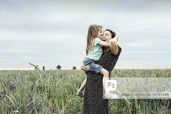 Glückliche Mutter und Tochter mit Feldblumenstrauß  die sich auf einer grünen Wiese umarmen. Mutter umarmt kleine Tochter im Freien auf einem Feld. Liebe und Familie Konzept
