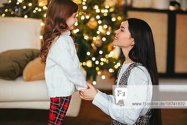 Glückliches verspieltes kleines Mädchen Tochter spielt mit positiven Mutter  verbringen Zeit zusammen während der Weihnachtsferien zu Hause  Mutter und Kind Spaß haben im Wohnzimmer mit Neujahr Baum