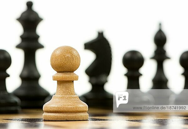 Weißer Baür gegen eine Übermacht von schwarzen Schachfiguren auf einem Schachbrett. Selektiver Fokus
