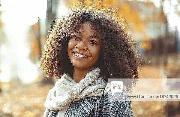Nette Herbst Nahaufnahme Porträt der jungen lächelnd glücklich afrikanischen amerikanischen Frau mit lockigem Haar genießen Spaziergang im Park im Herbst Saison. Outdoorfoto von zufriedenen schwarzen Mädchen mit Augen in der Liebe mit dem Leben