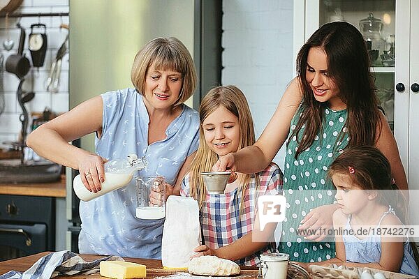 Glückliche erwachsene und reife Frauen kochen zusammen mit süßen Mädchen am Tisch in der Küche