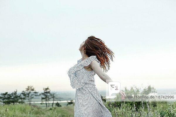 Seitenansicht einer jungen Frau  die ihr rotes Haar berührt und sich an einem Sommertag in der Natur ausruht