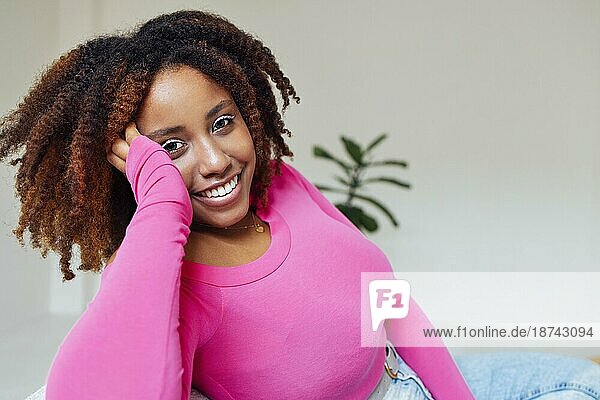 African American Millennial Mädchen  trägt rosa  zufrieden und ruhig  sitzt auf bequemen Sofa in gemütlichen modernen Wohnzimmer und hält Hand auf ihr Gesicht. Genießen Sie ihr Leben