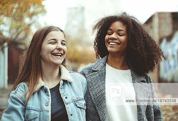 Zwei glückliche  sorglose  multirassische Freundinnen  die durch die Straßen der Stadt spazieren  sich unterhalten und Lebensgeschichten austauschen  multiethnische beste Freundinnen  die einen Herbstspaziergang im Freien genießen Frauen Freundschaft