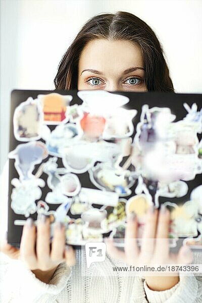Close up Foto von kaukasischen brunette Mädchen hält offenen Laptop in den Händen und schaut über Computerbildschirm in die Kamera mit runden großen blaün Augen schockiert  vor weißem Hintergrunden Wand. Selektiver Fokus