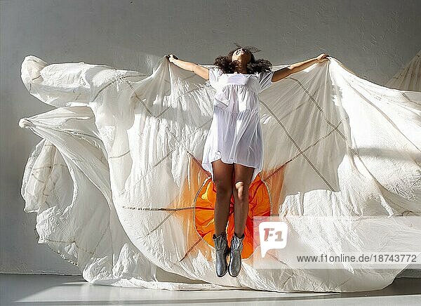 Springen und fliegen. Junge überglücklich sorglos afroamerikanische Frau springt in der Luft mit großen weißen Stoff isoliert über grauen Hintergrund Studio. Freiheit und Durst nach Leben Konzept