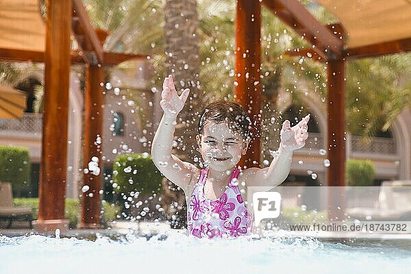 Adorable Mädchen im Badeanzug spritzt Wasser und haben Spaß im Schwimmbad im Sommer beim Blick in die Kamera