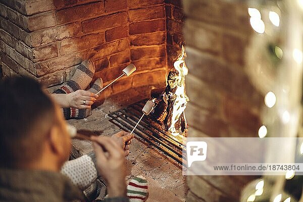 Glückliche junge Familie Eltern mit zwei kleinen Kindern versammeln sich um gemauerten Kamin in gemütlichen und warmen Landhaus während der Weihnachtsferien im Winter. Vater  Mutter und Kinder sitzen am Feuer zu Hause