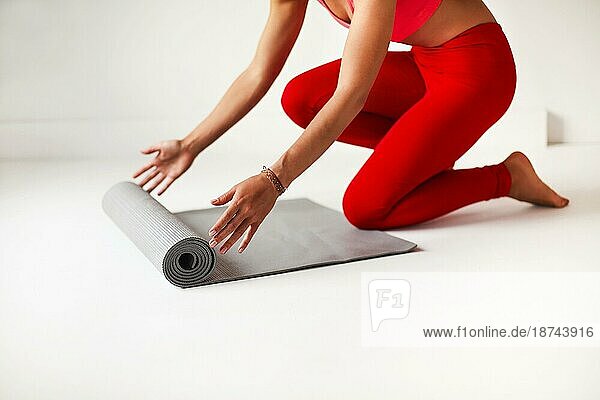 Seitenansicht der Ernte anonym schlanke Frau in leuchtend roten Top und Leggings Abrollen Matte für Yogapraxis in weißen Studio