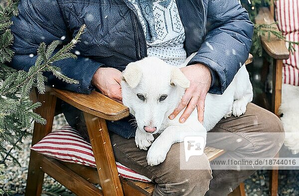 Mann und süßer weißer Hund sitzen auf Stühlen im Park an einem sonnigen Wintertag. Konzept der Freundschaft zwischen Tier und Mensch