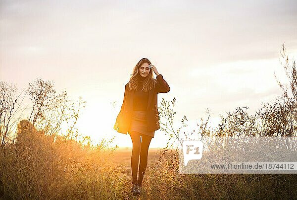 Junge glückliche kaukasische brünette Frau  die bei Sonnenuntergang über eine Wiese läuft und lächelt  verträumte schöne Frau im Abendsonnenlicht  die auf einem herbstlichen Feld auf dem Lande steht