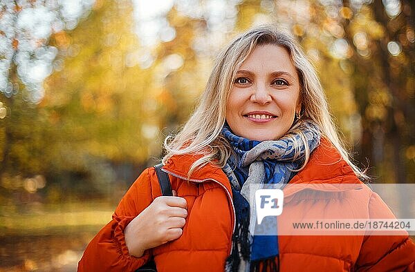 Zufriedene Frau in Oberbekleidung lächelnd an einem sonnigen Wochenendtag im Herbstpark