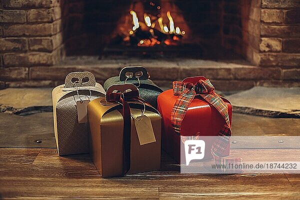 Frohe Weihnachten und ein gutes neues Jahr. Vier Weihnachtsgeschenke auf Holzboden in der Nähe von brennenden Kamin  niemand. Stapel von verpackten Weihnachtsgeschenken. Selektiver Fokus