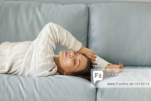 Porträt der entspannten positive junge brünette Frau liegt auf weichen blaün Sofa mit geschlossenen Augen  ziemlich lächelnd beim Entspannen in gemütlichen Hausumgebung. Menschen und Erholung Konzept