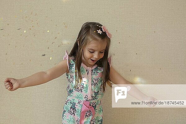Glückliche Kindheit. Aufgeregt ekstatisch niedlich liebenswert kleines Mädchen wirft Gold glänzend Konfetti in der Luft und lachen gegen beige Wand  Kind macht Spaß beim Spielen allein zu Hause