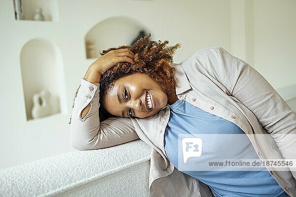 African American Millennial Mädchen  zufrieden und glücklich  sitzen auf bequemen Sofa in gemütlichen modernen Licht Wohnzimmer. Genießen Sie ihr Leben