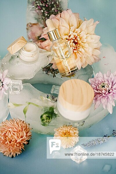 Natürliche Kosmetikprodukte und frische Blumen mit Eiswürfeln auf blauem Hintergrund angeordnet