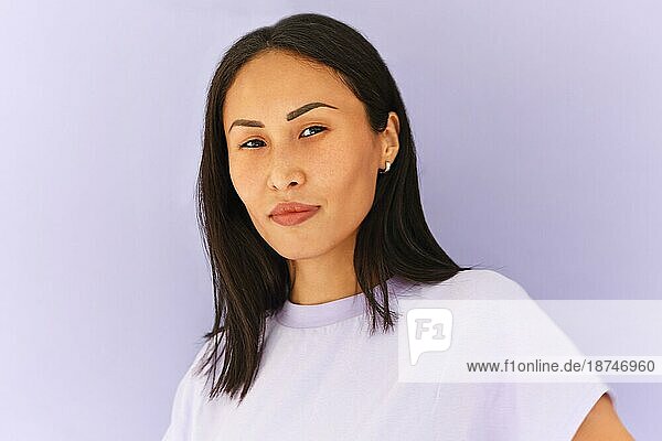 Positiv eingestellte asiatische Frau im Freizeithemd in einem hellvioletten Studio