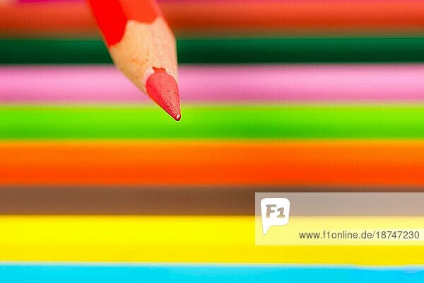 Spitze eines roten Holzbleistifts mit farbigen Buntstiften im Hintergrund selektiver Fokus