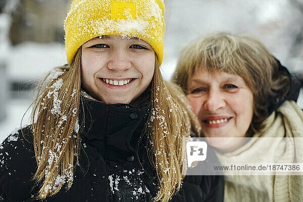 Lovely Porträt der glücklichen fröhliche Familie Großmutter und Enkelin in warmer Kleidung lächelnd glücklich in die Kamera  während Zeit im Freien im Winter auf kalten frostigen schneereichen Wetter. Selektiver Fokus