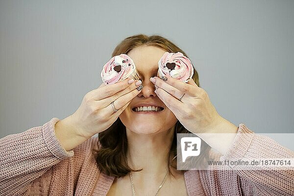 Erfreute weibliche Abdeckung Augen mit leckeren Cupcakes und lächelnd  während Sie Spaß gegen grauen Hintergrund