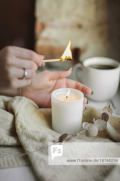 Weibliche Hände mit brennenden Streichholz Beleuchtung brennende Kerze auf der Fensterbank für Ruhe und Gemütlichkeit zu Hause  Frau versucht  gemütliche warme und intime Atmosphäre in der kalten Jahreszeit zu schaffen. Hygge Lebensstil Konzept