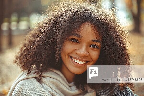 Cute Herbst Nahaufnahme Porträt der jungen lächelnd glücklich afrikanischen amerikanischen Frau mit lockigem Haar genießen Spaziergang im Park im Herbst Saison. Outdoorfoto von zufriedenen schwarzen Mädchen mit Augen in der Liebe mit dem Leben