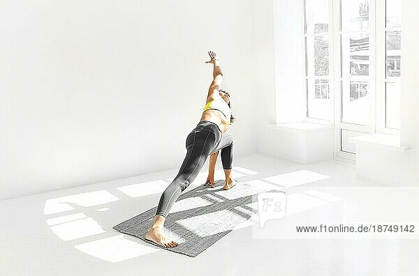 Seitenansicht einer ruhigen Frau in Sportkleidung  die Yoga in der Firefly Pose praktiziert  während sie auf den Armen auf der Matte balanciert und wegschaut